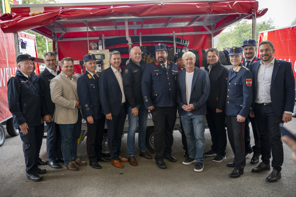 Feuerwehrleute und Zivilisten posieren vor einem roten Anhänger in Österreich